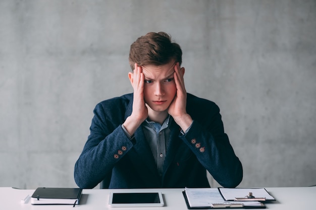 Rotina de escritório e prazos. Retrato de estressado jovem gerente sentado na mesa do escritório. Copie o espaço.