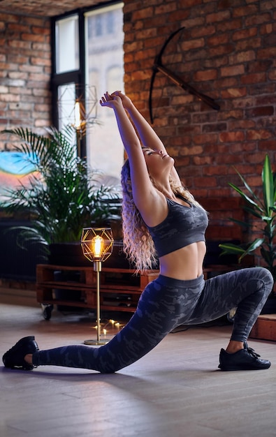 Rotina de exercícios de fitness da mulher. Mulher loira desportiva, estendendo-se em uma sala com interior loft.