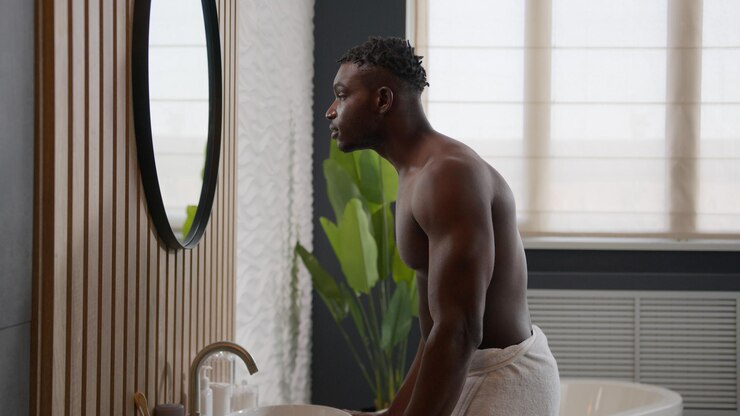 Foto rotina matinal de banheiro afro-americano atlético homem nu olhando para o espelho de banho