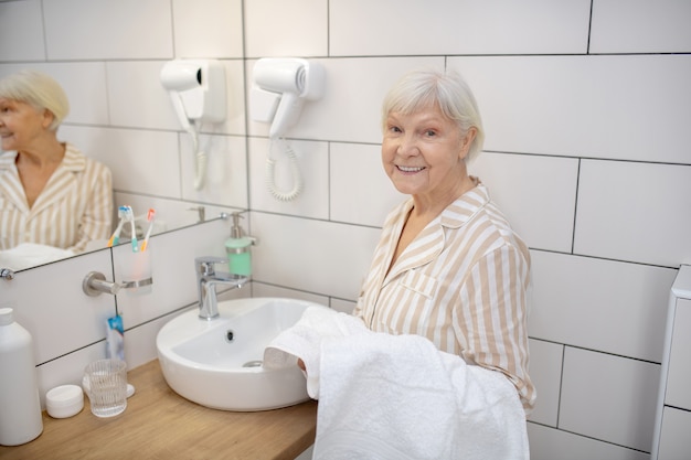 Foto rotina matinal. mulher grisalha no banheiro com uma toalha na mão