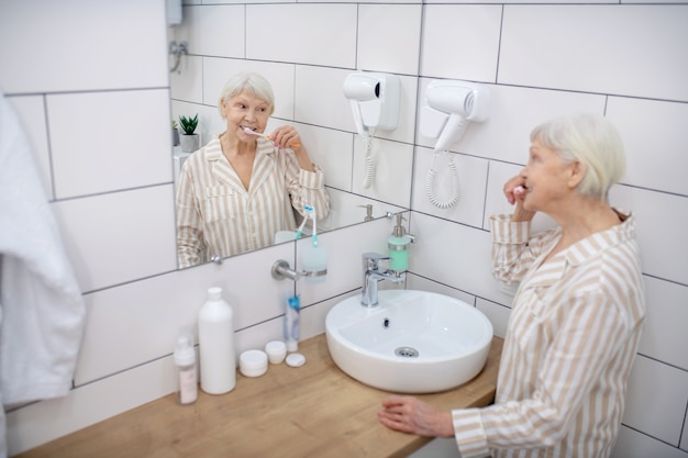 Rotina matinal. Mulher idosa escovando os dentes no banheiro