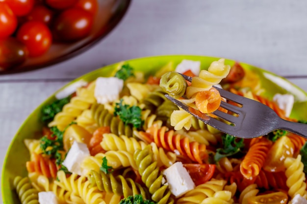 Rotini pasta italiana colorido con tomates cherry sobre fondo blanco de madera.