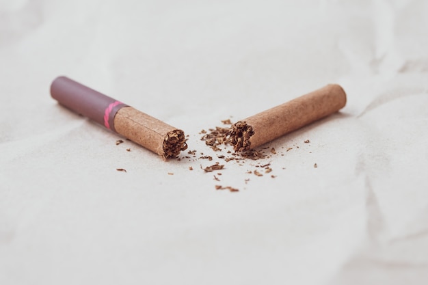 Roto puro oscuro sobre un fondo de papel neutro. Concepto de estilo de vida saludable Un cigarrillo aplastado y tabaco disperso. Copia, espacio de texto. Mal hábito, adicción a la nicotina. Día mundial sin tabaco.