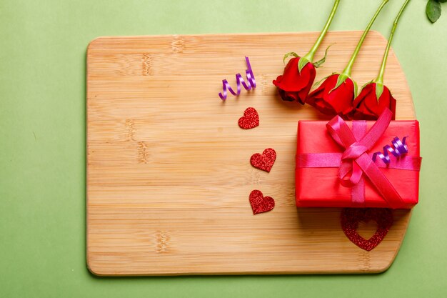 Rotrosenbündel und -geschenkbox auf hölzernem Brett. Valentinstag-Konzept