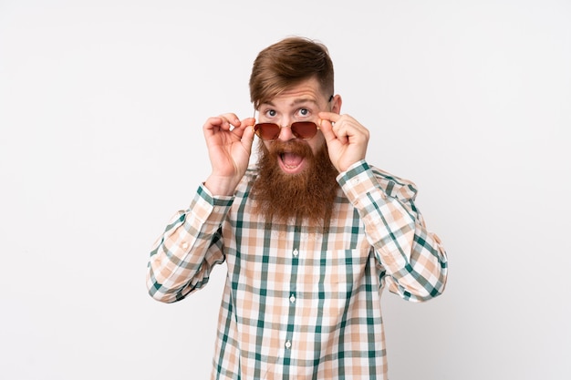 Rotschopfmann mit langem Bart über isolierter weißer Wand mit Brille und überrascht