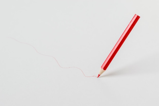 Rotstift, der eine Linie auf einem weißen Hintergrund zeichnet. Schreibwaren und Schulmaterial.