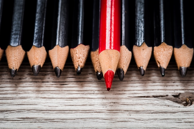 Rotstift hebt sich von der Menge des Schwarzen auf einem hölzernen weißen Hintergrund ab.