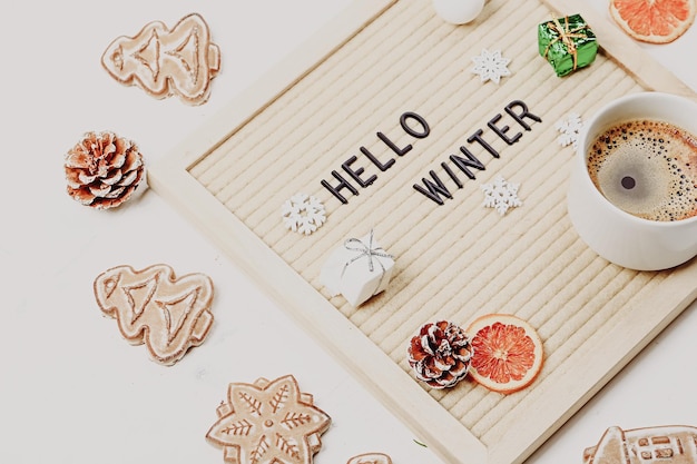 Foto rotulación hola invierno en tablero de letras ramas de abeto naranjas secas nueces y una taza de café fondo minimalista de año nuevo 2023