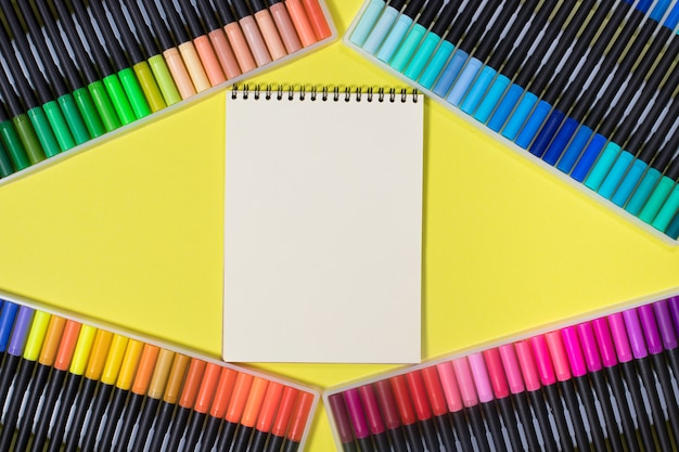 Rotuladores de colores y un cuaderno sobre un fondo amarillo con un lugar para el texto