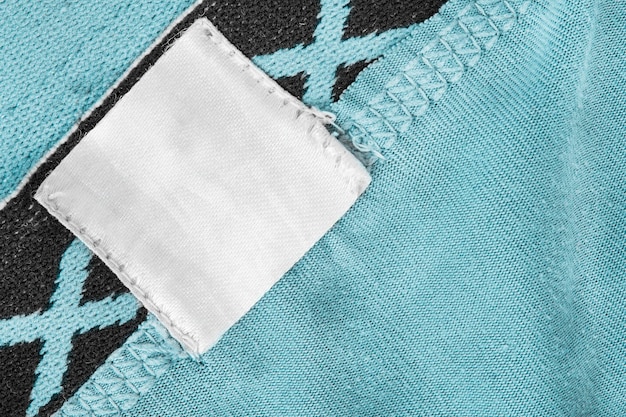 Rótulo de roupa em branco costurado em fundo de tecido azul