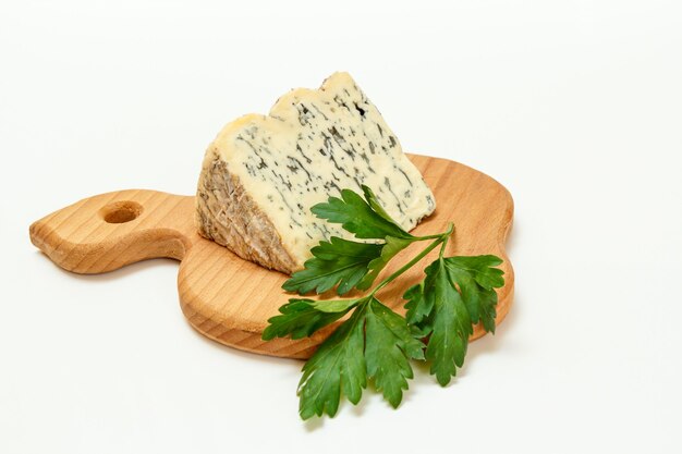 Rotura de Fourme d'Ambert, un queso azul francés semiduro y perejil fresco sobre una tabla de cortar de madera con la superficie blanca