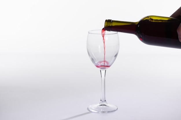 Rotwein gießt in Glas aus der Flasche auf weißem Hintergrund mit Kopierraum