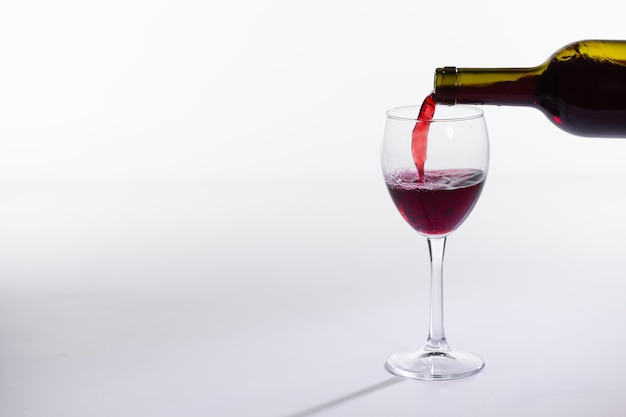 Rotwein gießt in Glas aus der Flasche auf weißem Hintergrund mit Kopierraum