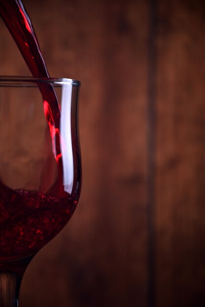 Rotwein in das Glas gegen hölzernen rustikalen Hintergrund gießen