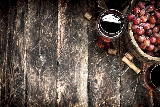 Rotwein mit einem Eimer Trauben auf Holztisch.