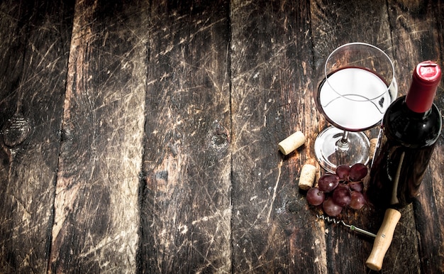 Rotwein mit einem Traubenzweig und einem Korkenzieher auf Holztisch.