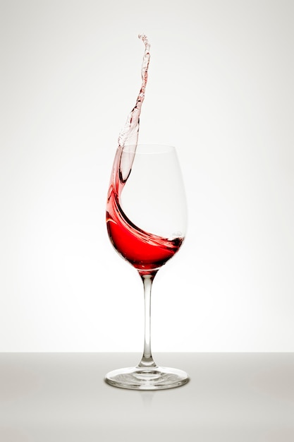 Rotwein spritzt im Glas vor weißem Hintergrund