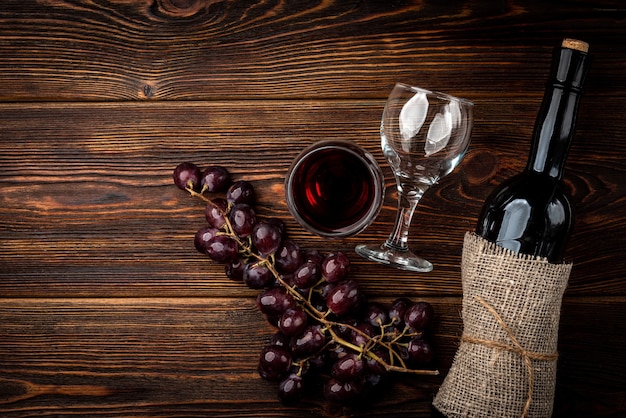 Rotwein und Traube auf dunklem hölzernem Hintergrund.