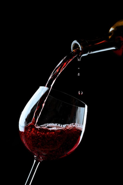 Rotwein wird in ein Weinglas auf schwarzem Hintergrund gegossen
