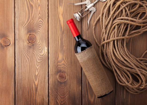 Rotweinflasche und Korkenzieher über rustikalem Holztischhintergrund mit Kopienraum
