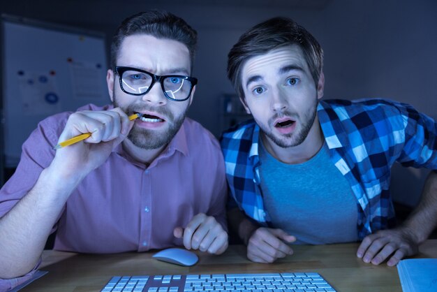 Roubando dados. Hackers espertos e nervosos sentados em frente ao computador e olhando para a tela enquanto roubam informações pessoais