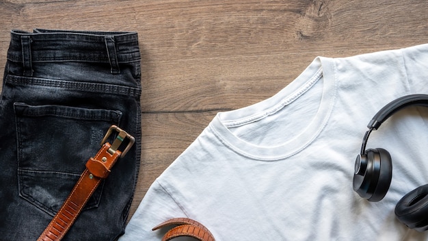 Foto roupa de roupa masculina em cima da mesa, camiseta, jeans, fones de ouvido e um cinto. vista do topo