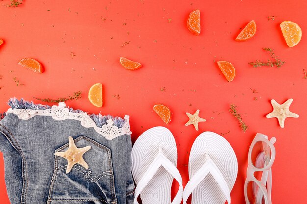 Roupa de verão das mulheres. Shorts jeans e chinelo branco e óculos de sol em fundo laranja. Postura plana. Copie o espaço.