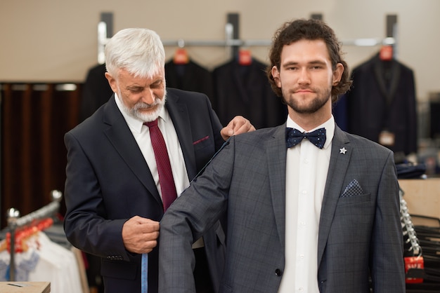 Roupa elegante, com cabelos grisalhos, medindo o braço e o ombro do cliente.