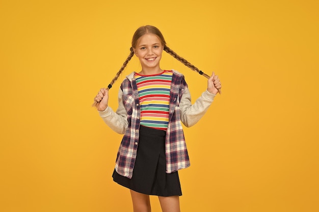 Roupas coloridas de menina pré-adolescente, loja de loja infantil, menina adorável, rosto bonito, salão de cabeleireiro, garotinha, criança pequena, com penteado de tranças fofas em fundo amarelo, conceito de cuidados infantis