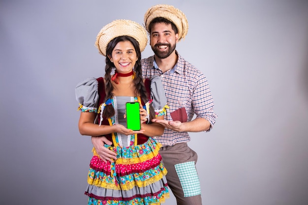 Roupas de casal brasileiro da festa junina arraial festa de sao joao namorado e namorada com tela verde do smartphone