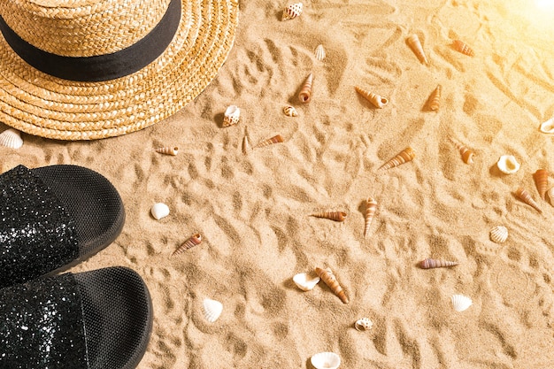 Roupas de praia de verão, chinelos, chapéu e conchas do mar na praia de areia.