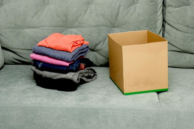 roupas dobradas ao lado de uma caixa vazia no sofá