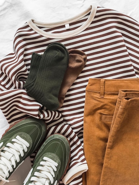 Foto roupas femininas aconchegantes em cores de outono, jeans de veludo, colete, tênis, meias em um fundo claro, vista superior