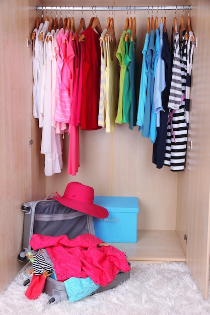 Roupas femininas no guarda-roupa e mala no quarto.