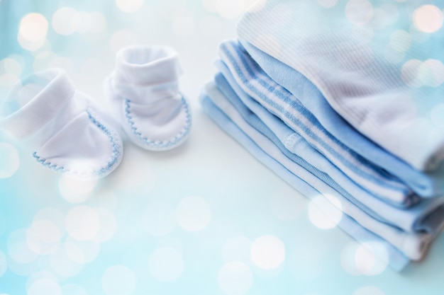 roupas, infância, maternidade e conceito de objeto - close-up de sapatinhos de bebê na pilha de roupas dobradas para menino recém-nascido