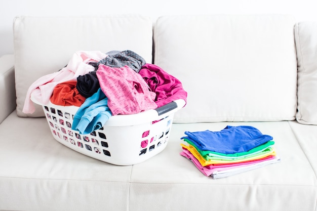 Roupas lavadas em uma cesta e uma pilha de lençóis limpos no sofá