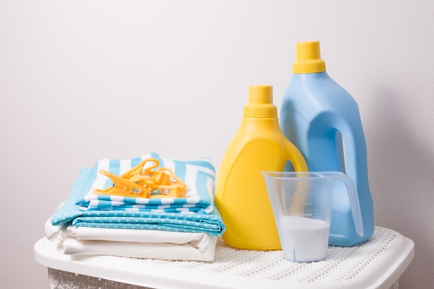 roupas, sabão em pó no copo medidor e géis de lavagem em amarelo e garrafas na cesta de plástico