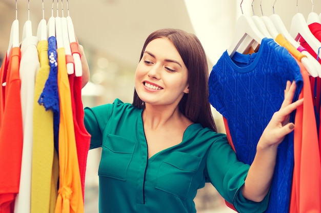 roupas, venda, moda, estilo e conceito de pessoas - mulher feliz escolhendo roupas no shopping ou shopping