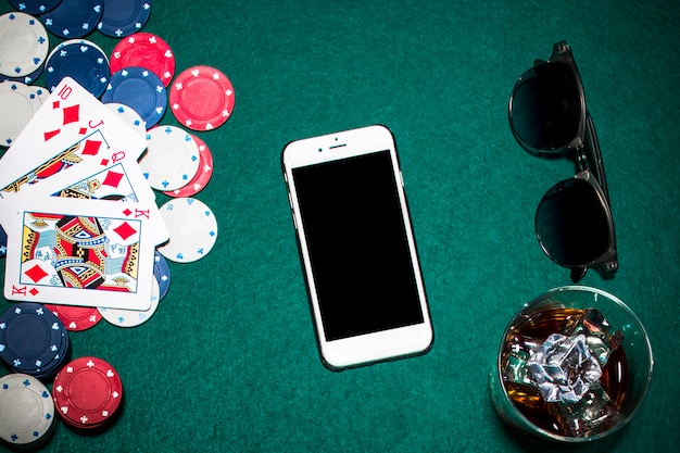 Royal Flush baralho; fichas de casino; celular; óculos de sol e copo de uísque sobre o fundo de poker