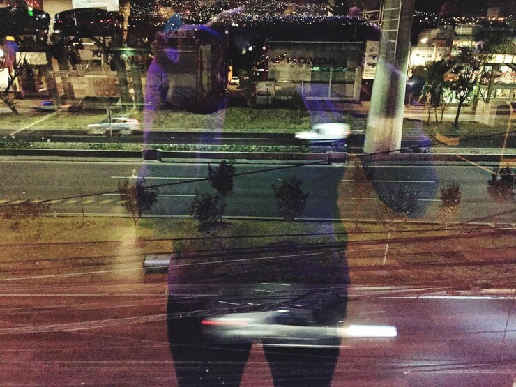 Foto rua da cidade vista através de uma janela de vidro com o reflexo de uma pessoa à noite