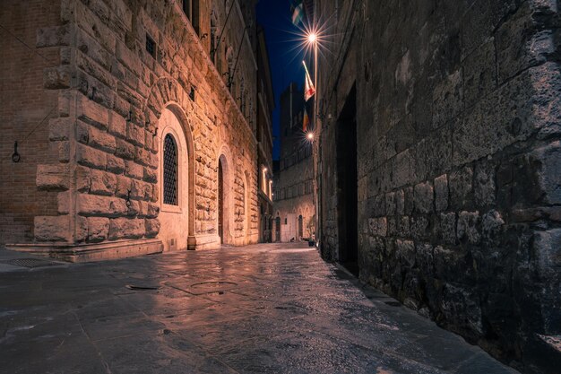 Rua medieval estreita e escura no centro histórico à noite com luzes raras Siena Itália