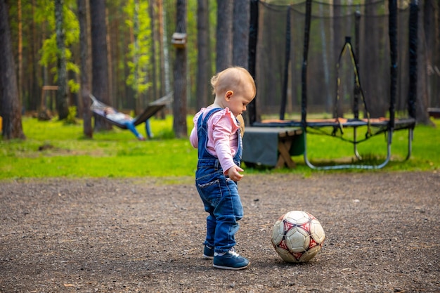 Rubia bebé niña activa jugando con pelota de fútbol en el bosque Rusia