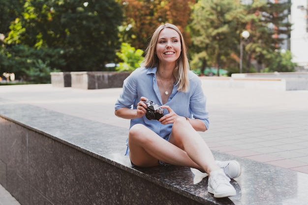 Rubia encantadora joven tomando fotografías en la calle con una cámara retro