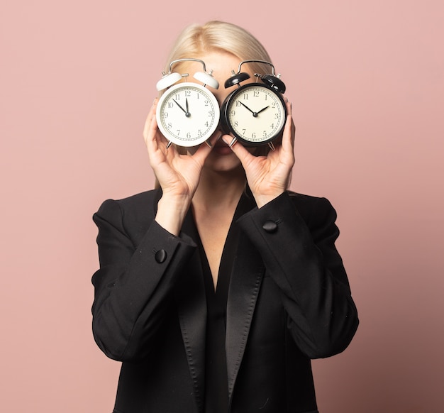 Rubia de estilo en chaqueta y gafas de sol con despertadores en rosa