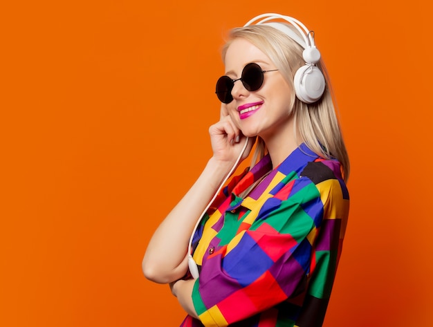 Rubia de estilo con ropa de los 90 con auriculares en naranja