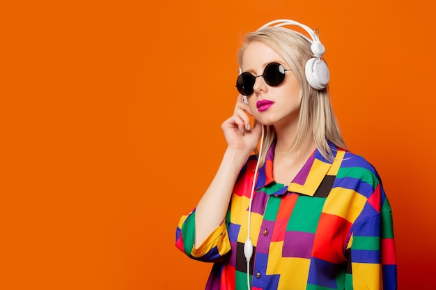 Rubia de estilo con ropa de los 90 con auriculares en naranja