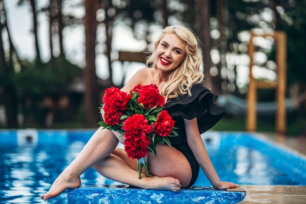 Rubia con estilo en traje de baño vintage negro relajante en la piscina al aire libre