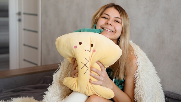 Rubia feliz bajo una manta blanca por la mañana abraza una almohada amarilla. Concepto de feliz mañana