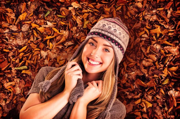 Foto rubia feliz en ropa de invierno posando contra hojas de otoño en el suelo
