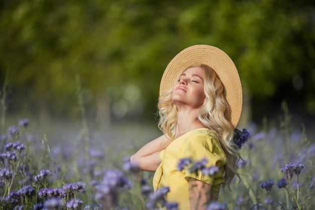 Rubia joven hermosa mujer con un sombrero camina por un campo de flores de color púrpura. El verano. Primavera.